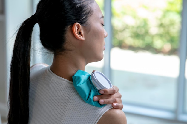 Asian woman putting a hot water bag on her shoulder pain