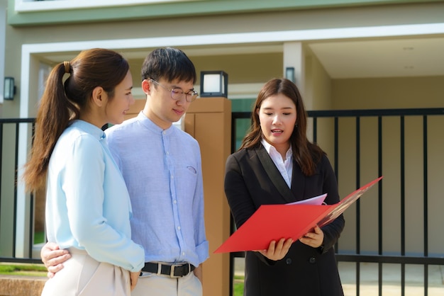 Asian woman Real estate broker agent showing a house detail in her file to the young Asian couple lover looking and interest to buy it Buying a new housexA