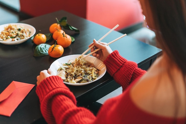 Photo asian woman in red clothes eating noodles with bamboo chopsticks in chinese vietnamese restaurant