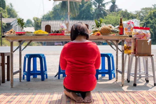 Asian woman red shirt sitting and praying to ancestor with mealdessert and beverage on table in new year chinese