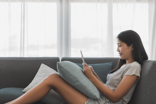 Asian woman relax and using mobile phone on sofa in living room at home