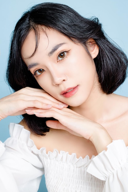 Asian woman short hair with Perfect clean fresh skin Cute female model with natural makeup and sparkling eyes on blue isolated background Facial treatment Cosmetology beauty Concept