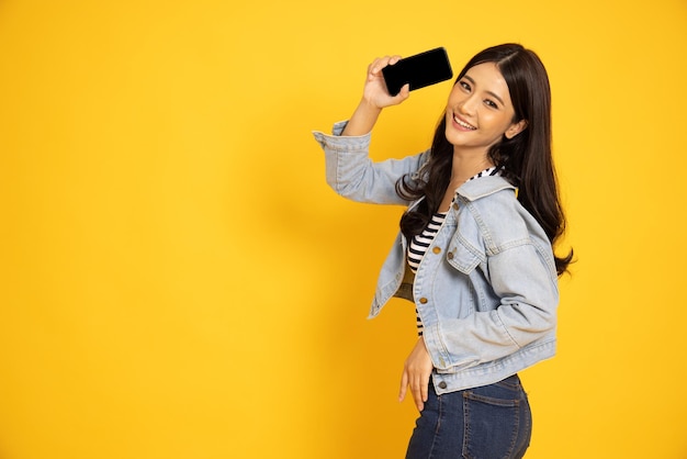 Asian woman showing or presenting mobile phone application isolated over yellow background