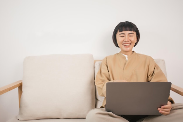 Asian woman sit on couch and watch funny movie on laptop