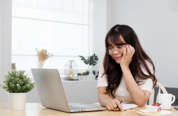 Asian woman Sit at your desk Looking at laptop computers with a smile, working from home.