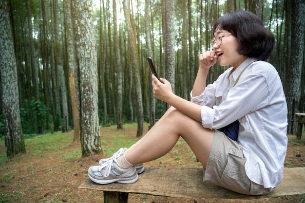 Asian woman sitting on the bench using a mobile phone in the forest