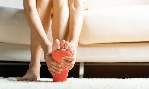 Asian woman sitting on sofa feeling pain in her foot at home