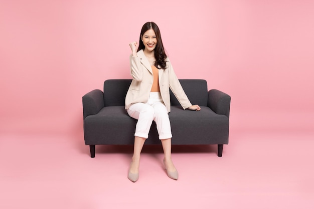 Asian woman sitting on sofa and hands up raised arms from happiness Excited