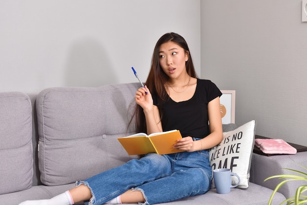 Asian woman sitting on sofa and orange copybook