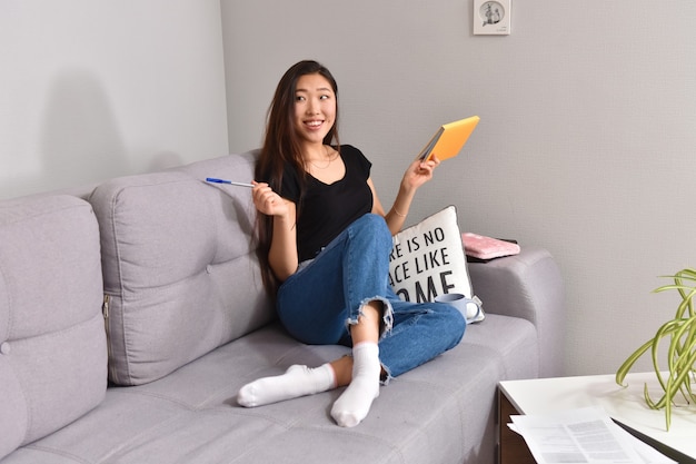 Asian woman sitting on sofa and orange copybook