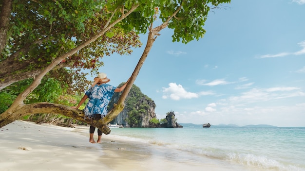 Asian woman sitting on the tree and enjoying with beautiful sea nature in her vacation.