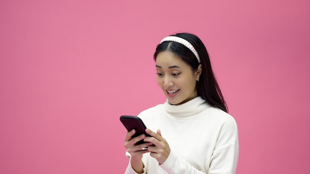 Asian woman smiling and using mobile phone with tablet and excited for online shopping on isolated pink background