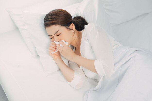 Asian woman sneezing on bed