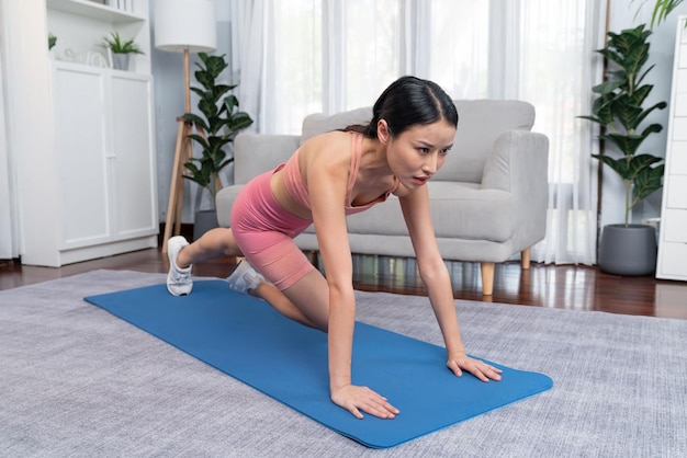 Asian woman in sportswear doing burpee on exercising mat as home workout training routine Attractive girl engage in her pursuit of healthy lifestyle and fit body physique Vigorous