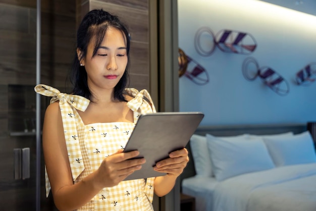 Asian woman standing using digital tablet Smile lady browsing internet over tablet at home Smart woman read text on her digital tablet during recreation time at home