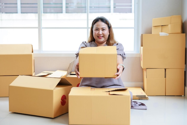 Asian woman startup packaging business holding parcel box order by online at her home