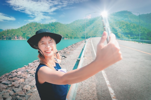 Asian woman in summer dresses is taking selfie using mobile phone on a beautiful beach