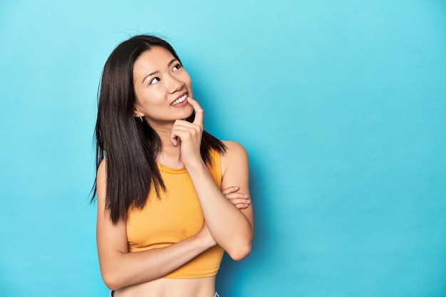 Asian woman in summer yellow top studio setup relaxed thinking about something