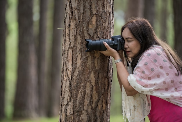 Photo asian woman taking photo with dslr, shooting pose with tree concept.