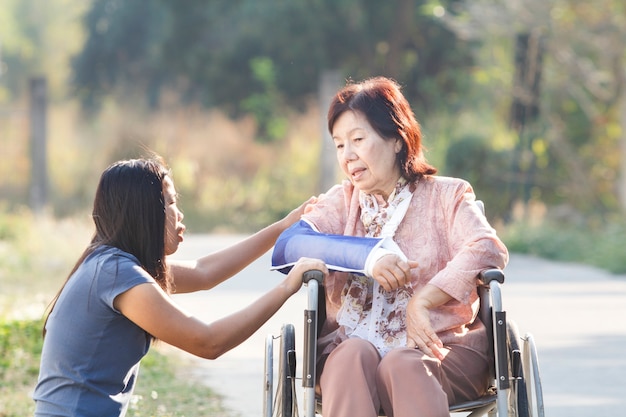 Asian woman taking their disable senior mother for a walk at the park ,Thailand