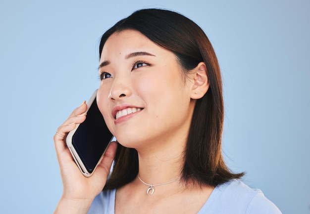 Asian woman thinking and phone call in studio with chat networking and smile by blue background Young Japanese student girl and smartphone for contact mobile connection and memory with ideas