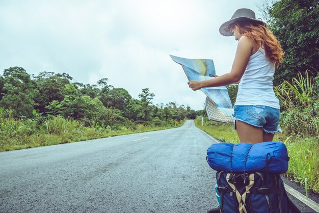 Asian woman travel relax. Take a look at the map on a rural road in the middle of nature.