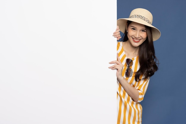 Asian woman traveler is standing behind the white blank banner on blue background Looking at camera