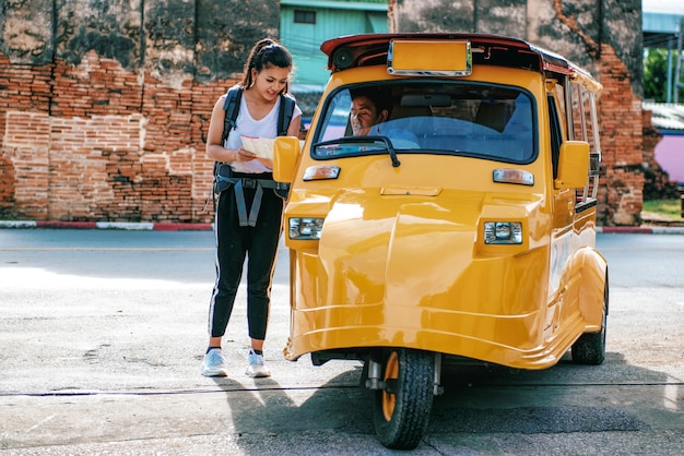 Asian woman travelers ask Tuk-Tuk driver about right direction on the map while exploring travel. At Ayutthaya historical park Thailand.