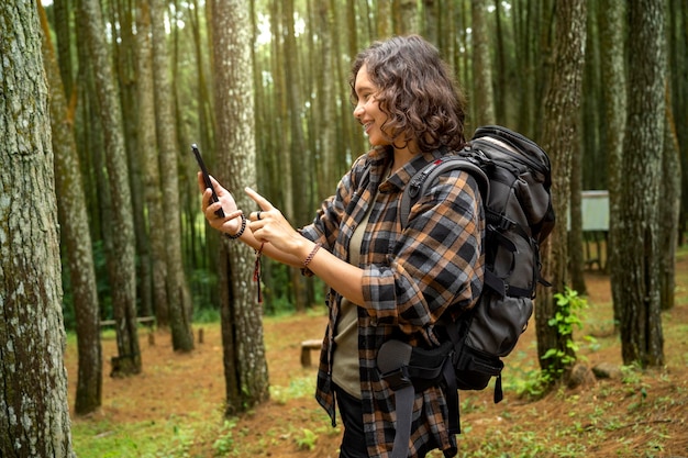 Asian woman trekking while using mobile phone in the forest