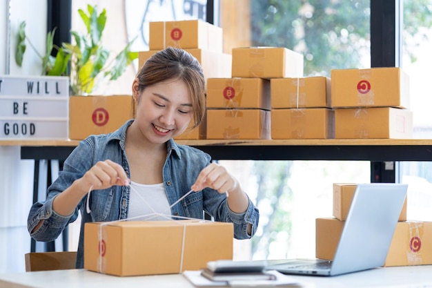 An Asian woman tying a parcel to a customers box she owns an online store she packs and ships through a private transport company Online selling and online shopping concepts