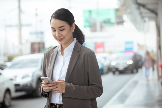 Asian woman use smartphone standing against street blurred building background