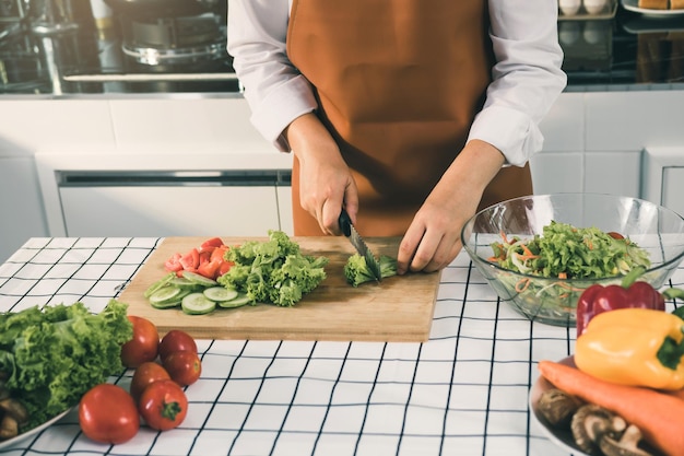 Asian woman uses a knife to cut the salad greens in the kitchen