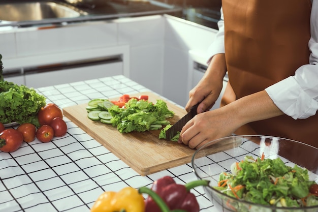 Asian woman uses a knife to cut the salad greens in the kitchen