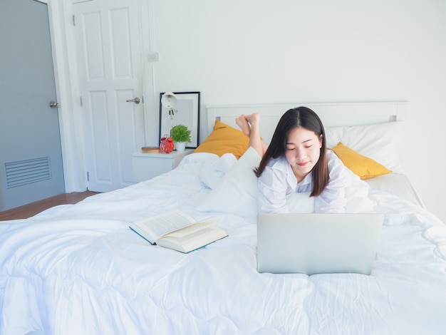 Asian woman using computer and read book on bed in the morning