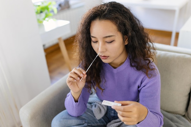 Asian woman using cotton swab while doing coronavirus PCR test Woman takes coronavirus sample from her nose at home woman at home using a nasal swab for COVID19