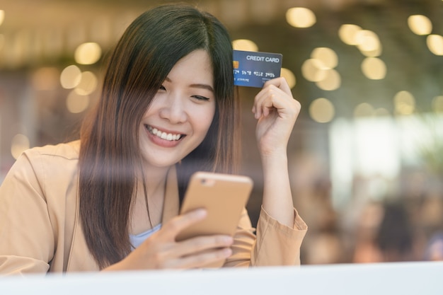 Asian woman using credit card with mobile phone for online shopping in department store