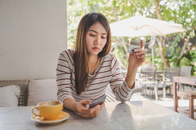 Asian Woman using credit or debit card by application on smartphone for payment online