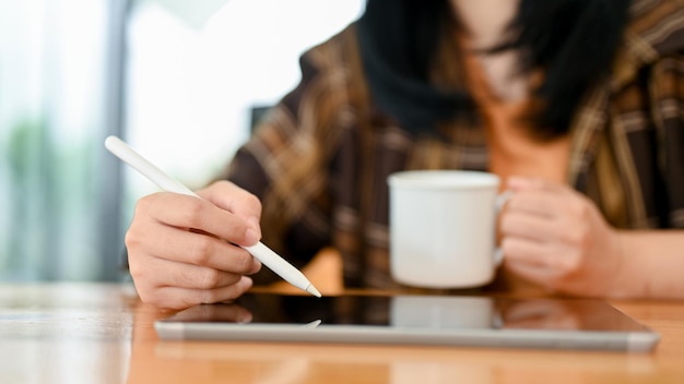 An Asian woman using digital tablet while sipping coffee in the coffee shop remote working