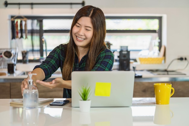 Asian woman using hand sanitizer when working at home with technology laptop