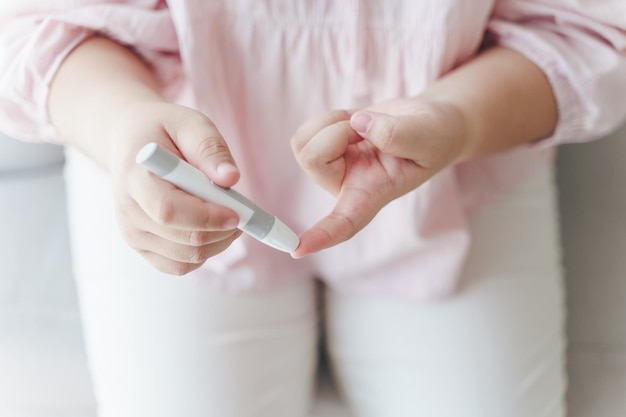 Asian woman using lancet on finger for checking blood sugar level by Glucose meter