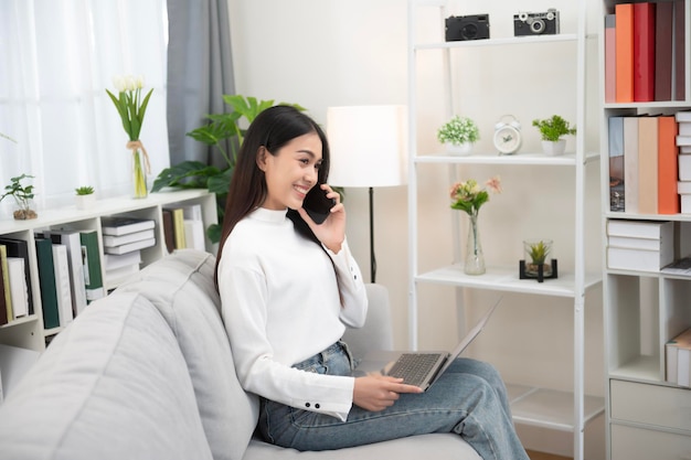 Asian woman using mobile phone with positive expression big smile casual dress and sitting on white background sofa Lovely happy woman congratulating success