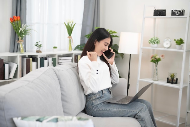 Asian woman using mobile phone with positive expression big smile casual dress and sitting on white background sofa Lovely happy woman congratulating success