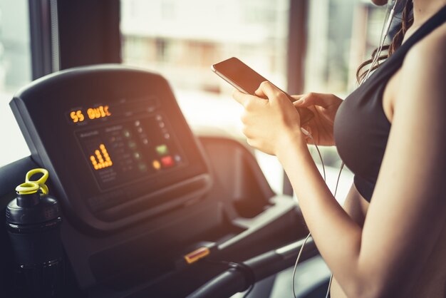 Asian woman using smart phone when workout or strength training at fitness gym on treadmill