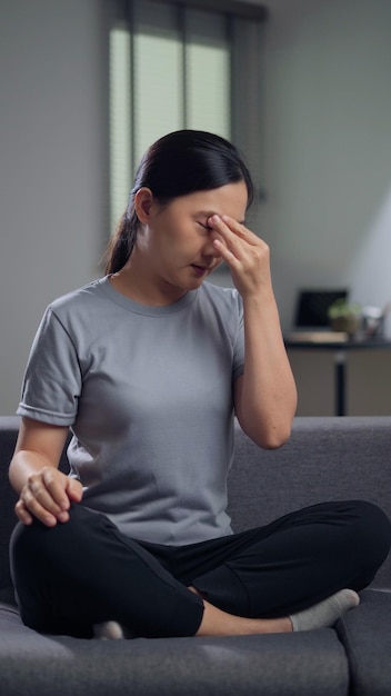 Asian woman was sick with eyes pain irritate itching her eyes sitting on sofa in living room at home