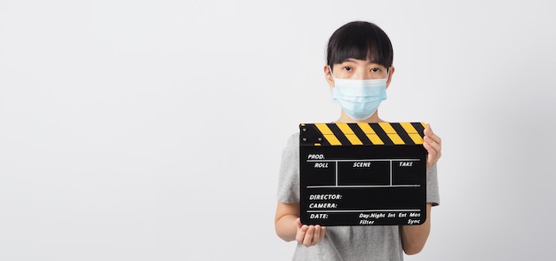 Asian woman wear face mask and hand's holding black clapper board or movie slate or clapboard use in video production film cinemamovies industry on white background