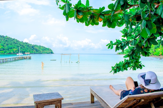 Asian woman wear hat with smartphone sitting seaside