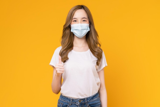 Asian woman wear masks to protect disease and showing thumbs up or like on yellow background.