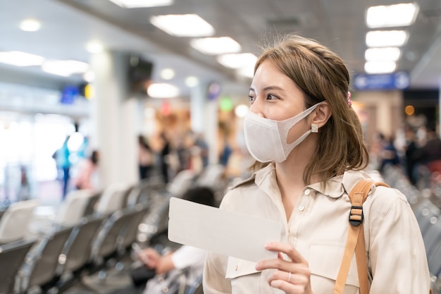 Asian woman wear masks while traveling, holding boarding pass at the airport terminal