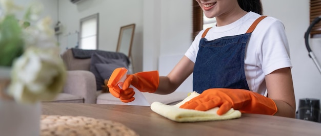 Asian woman wear rubber protective orange gloves sit clean guest reception desk with product and equipment cleaner at home