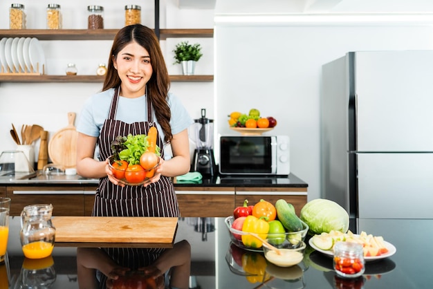 Asian woman wearing apron preparing a healthy salad with vegetables.